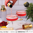 Load image into Gallery viewer, Champagne being poured into red cocktails served in ribbed coupe glasses with gold rim and matching cocktail shaker.