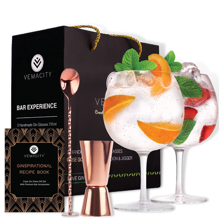 A set of handcrafted crystal gin glasses with bar accessories including a bar spoon, shot measure, and a recipe e-book, presented in a black gift box with gold accents.