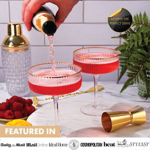 Champagne being poured into red cocktails served in ribbed coupe glasses with gold rim and matching cocktail shaker.