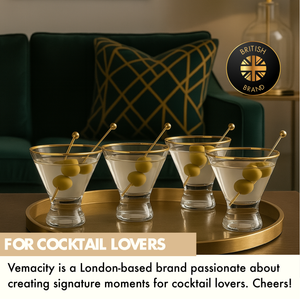 Four Vemacity stemless martini glasses with gold rims and olives on cocktail sticks, displayed on a tray in a modern living room setting.